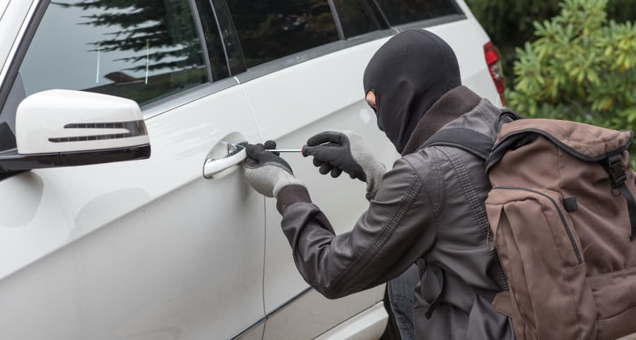 Thief attempting to break into a white automobile in a residential neighborhood