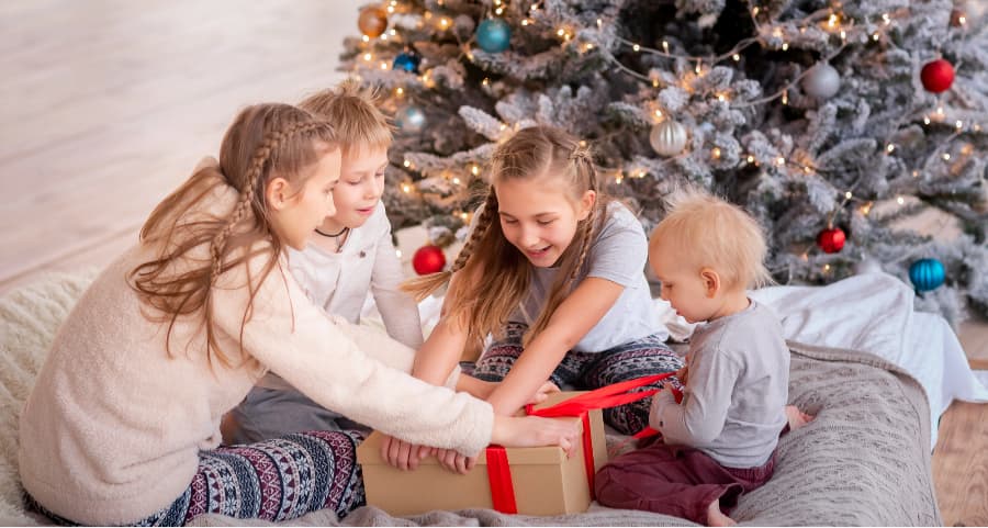 Children opening a gift in the living room next to a Christmas tree.